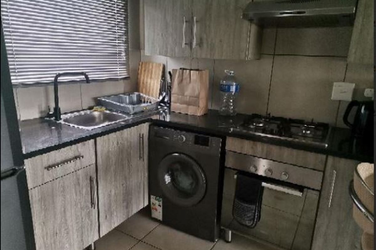 Compact kitchen featuring modern laminate cabinetry, granite countertops, built-in oven with gas hob, extractor fan, and an integrated washing machine.