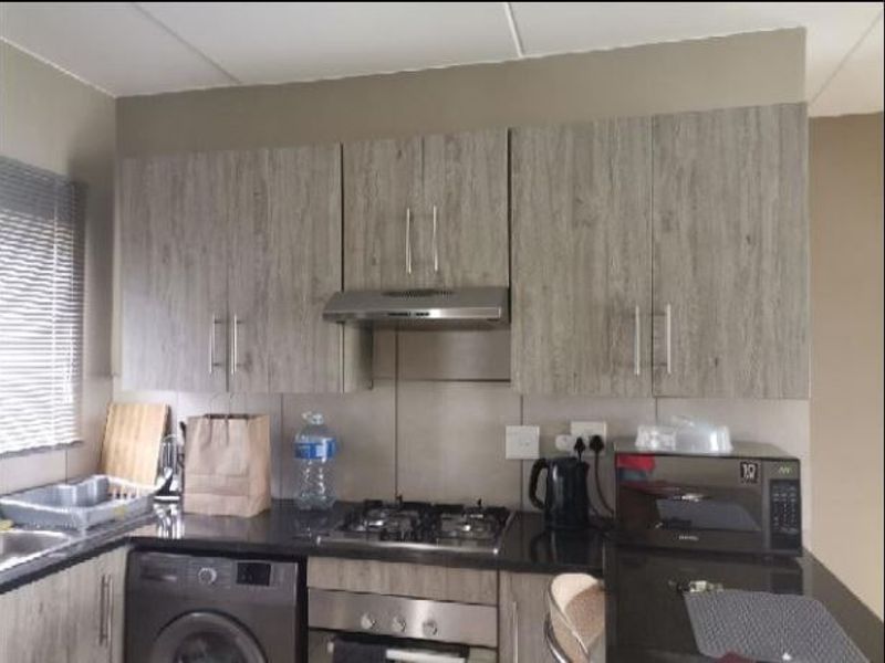 A functional kitchen featuring modern wood-grain cabinetry, granite countertops, a gas hob, built-in oven, extractor fan, and an integrated washing machine.
