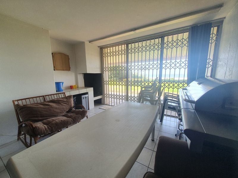 Covered patio area featuring a built-in braai, tiled flooring, and security gates leading to an outdoor garden space.
