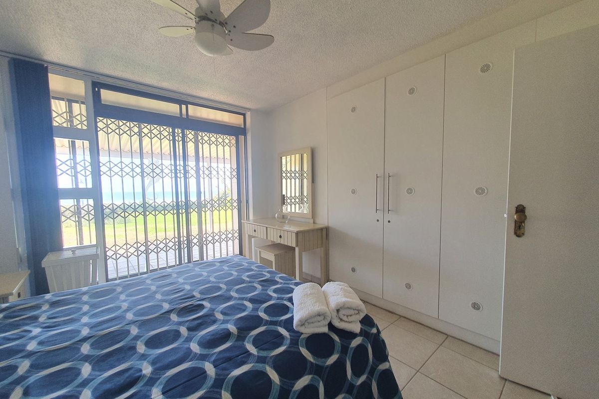 A bedroom featuring built-in cupboards, a ceiling fan, tiled flooring, and a sliding glass door with a security gate leading to an outdoor area.