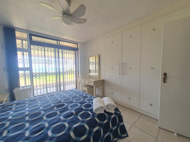 A bedroom featuring built-in cupboards, a ceiling fan, tiled flooring, and a sliding glass door with a security gate leading to an outdoor area.
