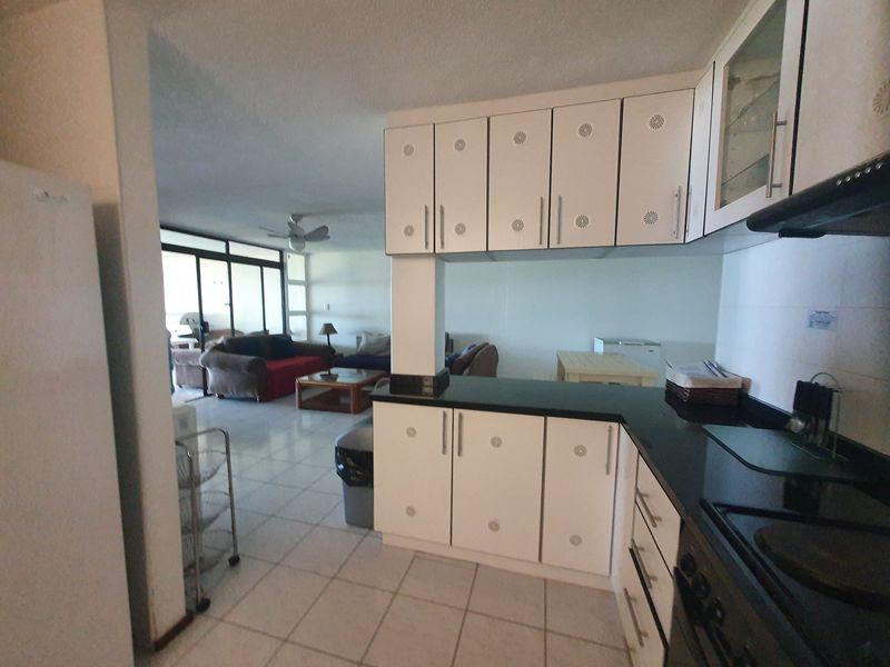 Open plan kitchen and living area featuring white cabinetry, black granite countertops, and ceramic floor tiles, creating a functional and connected living space.