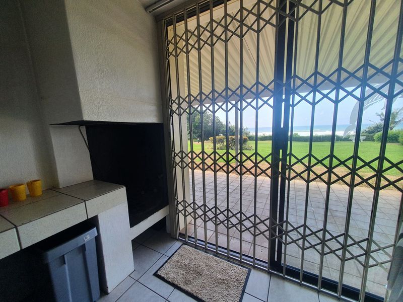 Covered patio area featuring a built-in braai, tiled flooring, and sliding glass doors with security gates, offering direct access to the garden and ocean views.