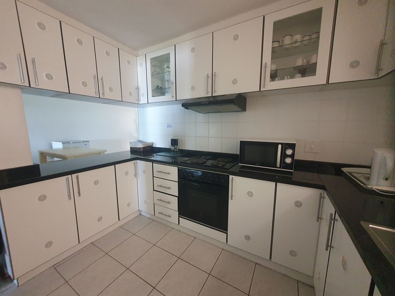 A functional kitchen featuring white cabinetry, black granite countertops, a built-in oven, electric hob, and tiled flooring with a clean, neutral aesthetic.