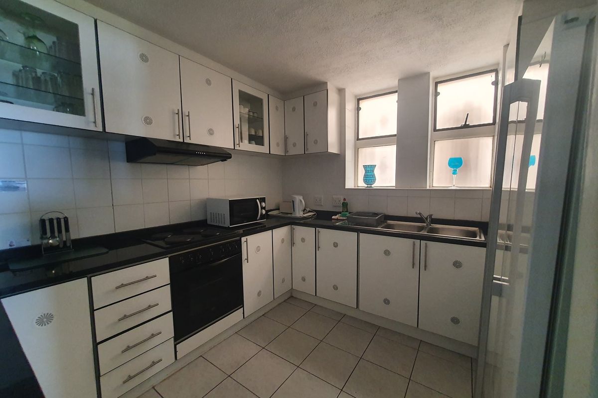 Functional kitchen featuring white cabinetry, black granite countertops, built-in oven, electric hob, and a double bowl stainless steel sink with tiled finishes.