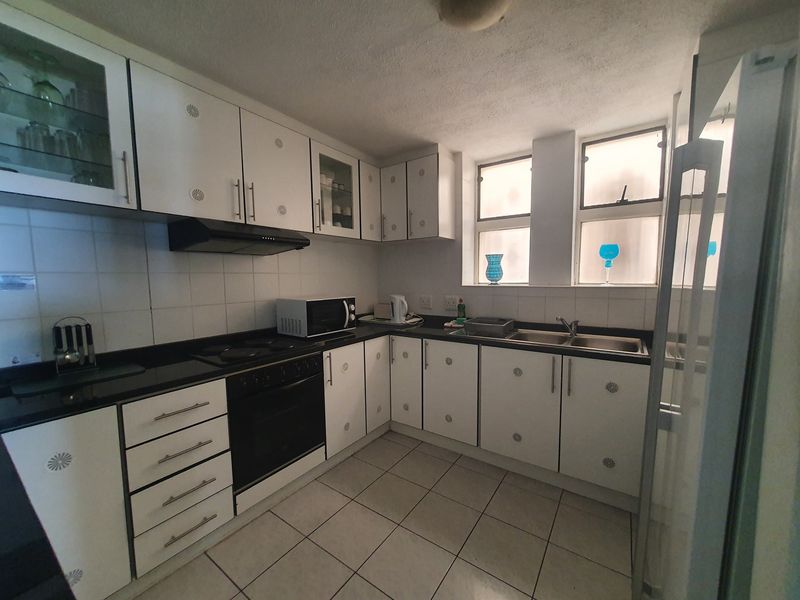 Functional kitchen featuring white cabinetry, black granite countertops, built-in oven, electric hob, and a double bowl stainless steel sink with tiled finishes.