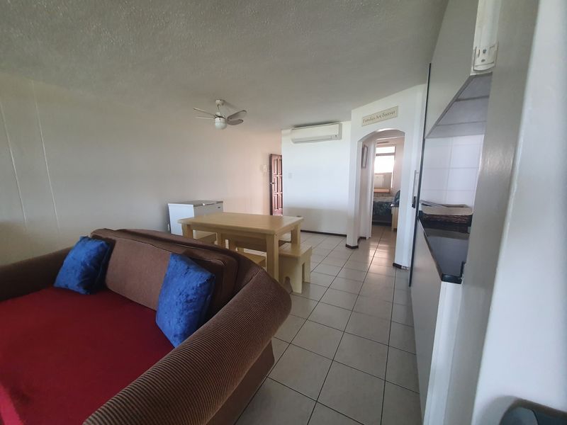 Open-plan living and kitchen area featuring tiled flooring, a ceiling fan, and a wall-mounted air conditioning unit.