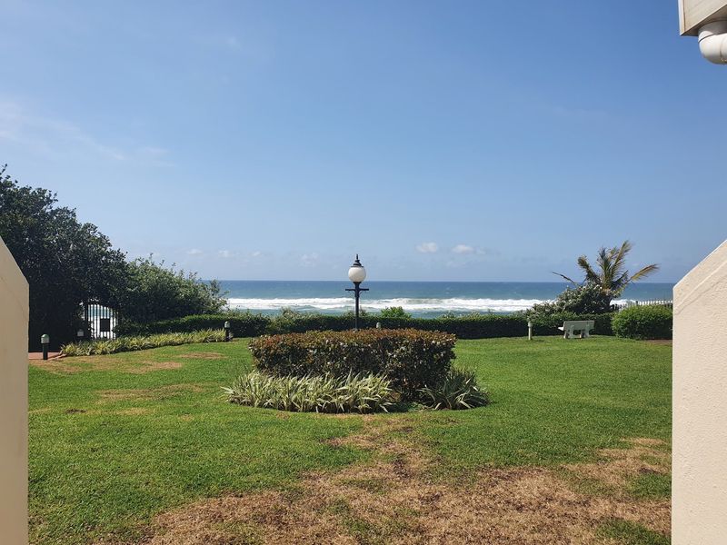 A scenic view of the ocean from a well-maintained communal garden area featuring manicured lawns and established landscaping.