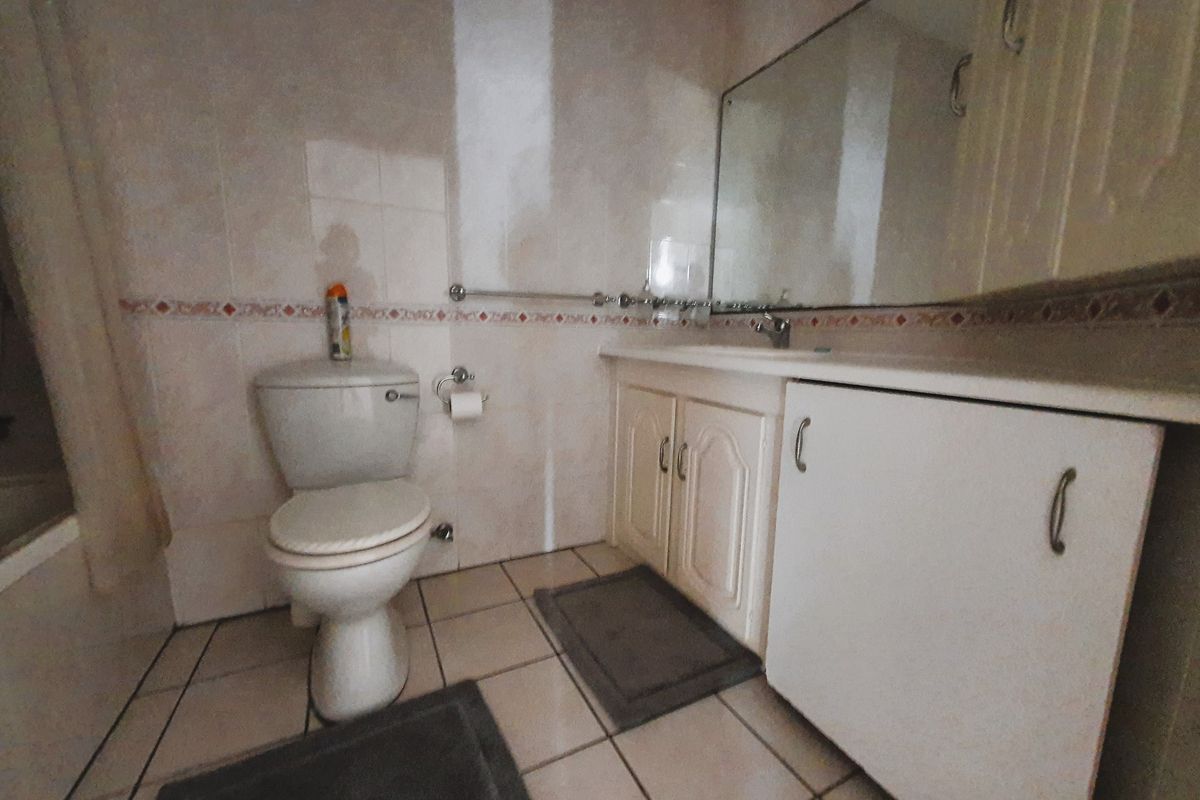 A functional bathroom featuring a vanity cabinet with storage, a wall-mounted mirror, and tiled surfaces throughout.