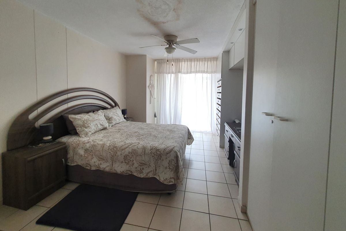A bedroom featuring tiled flooring, built-in cupboards, and a ceiling fan, with visible water damage on the ceiling requiring attention.