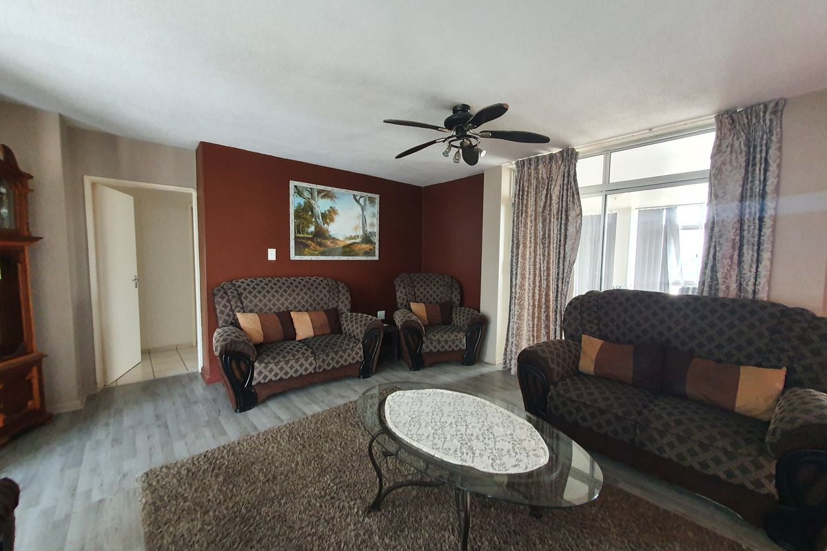 A spacious living room featuring laminate flooring, a ceiling fan, and large glass sliding doors that provide ample natural light.