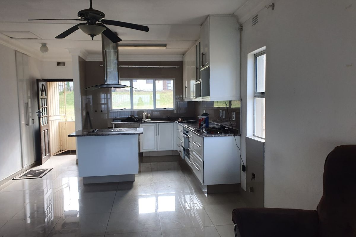 A functional kitchen featuring white cabinetry, a central island, granite countertops, and a stainless steel extractor fan, with tiled flooring throughout.