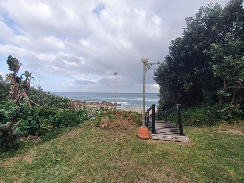 A scenic outdoor view featuring a wooden staircase leading towards the beach, surrounded by natural landscaping and coastal vegetation.