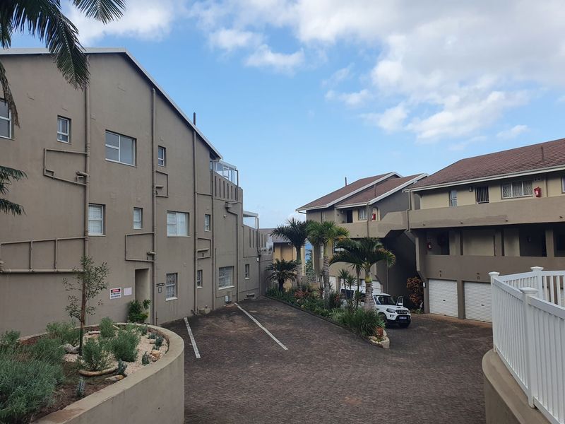 Exterior view of an apartment complex featuring a paved driveway, multiple garage units, and landscaped garden areas.