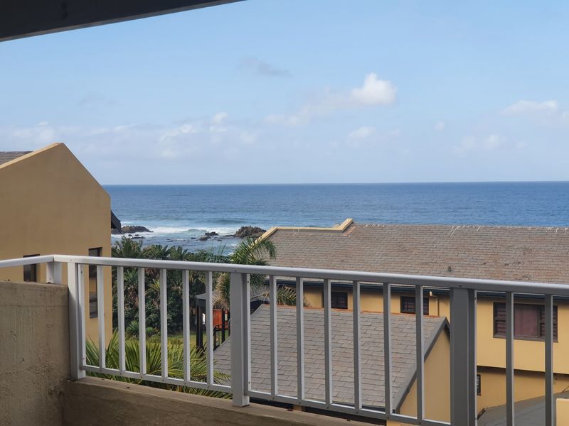 A balcony featuring a white metal balustrade with an expansive view of the ocean and surrounding residential rooftops.