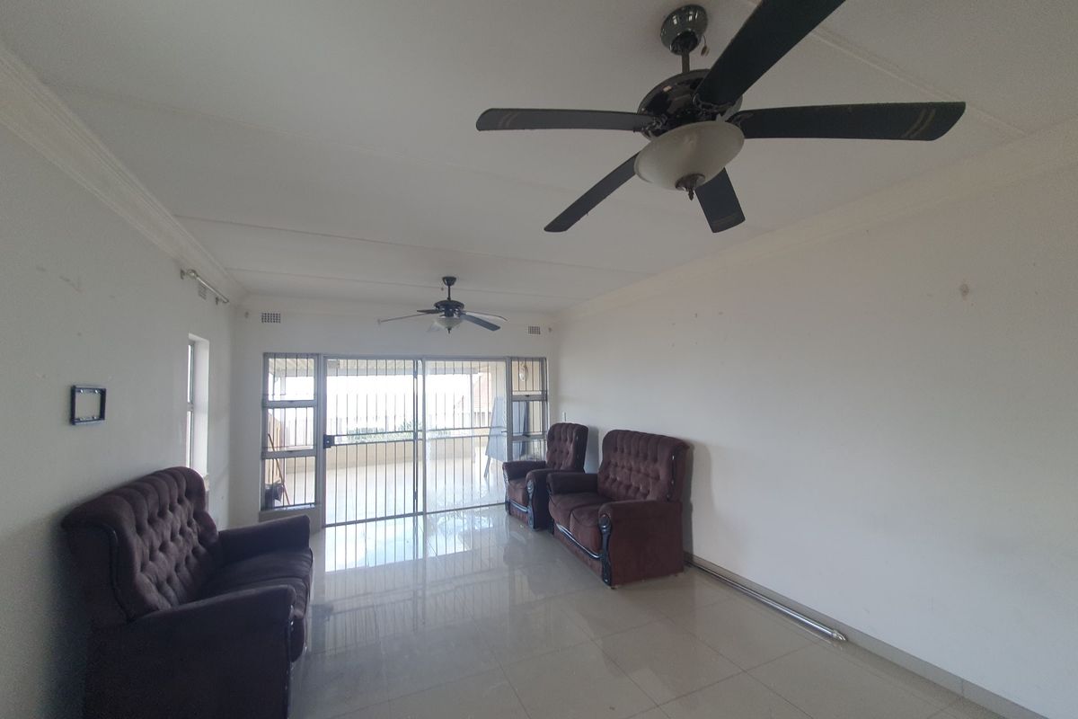 Spacious living area featuring tiled flooring, dual ceiling fans, and a sliding glass door with security gate leading to an outdoor space.