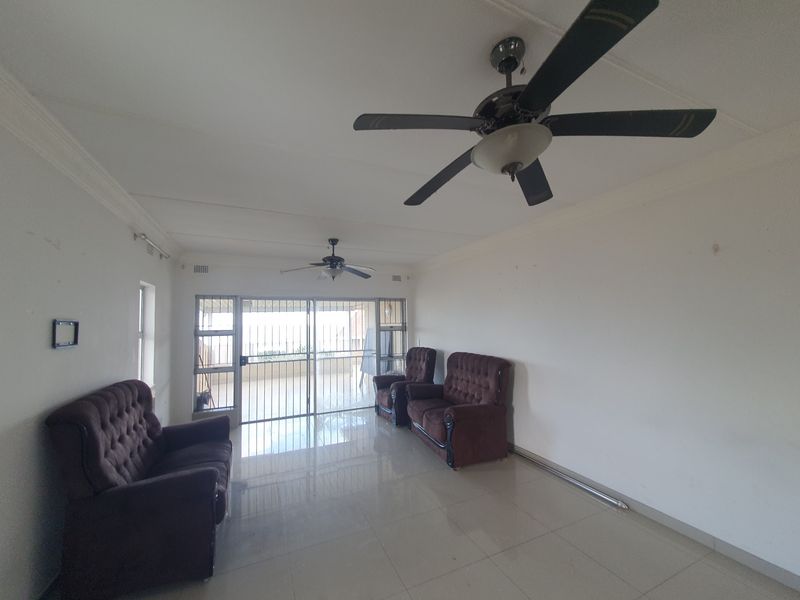 Spacious living area featuring tiled flooring, dual ceiling fans, and a sliding glass door with security gate leading to an outdoor space.