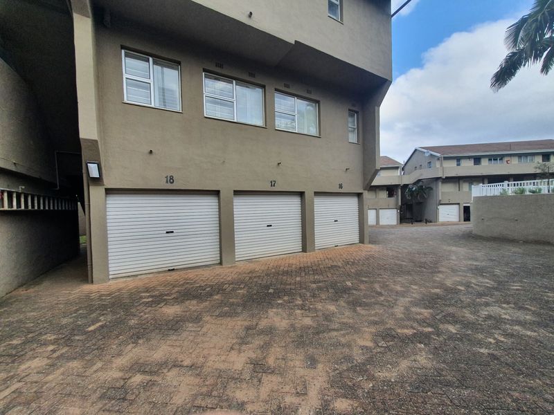 Exterior view of an apartment complex featuring three individual roller shutter garage doors and a paved driveway area.