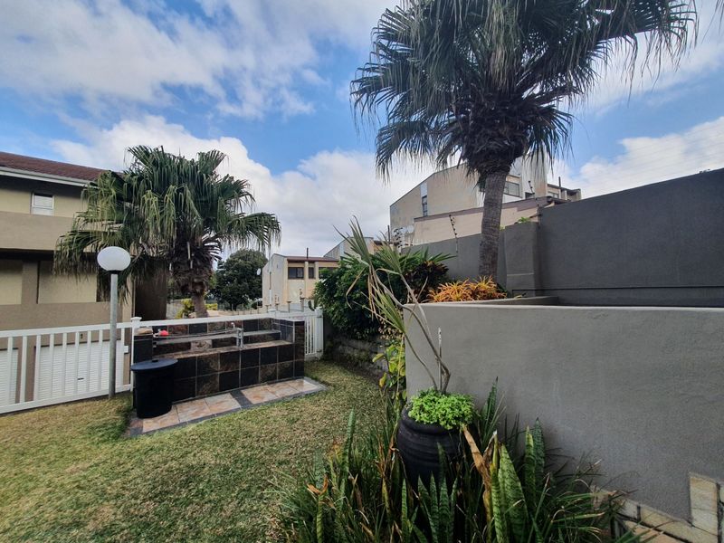 A private rear garden area featuring a built-in tiled braai station, established palm trees, and perimeter boundary walls.