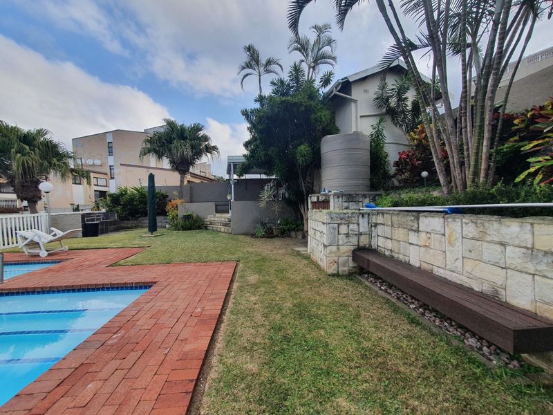 Outdoor pool area featuring brick paving, a stone retaining wall with built-in bench seating, and a water tank in a landscaped garden setting.