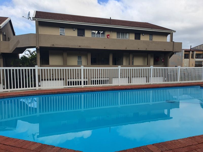 A well-maintained apartment complex featuring a clear swimming pool with brick coping and a white picket fence enclosure.