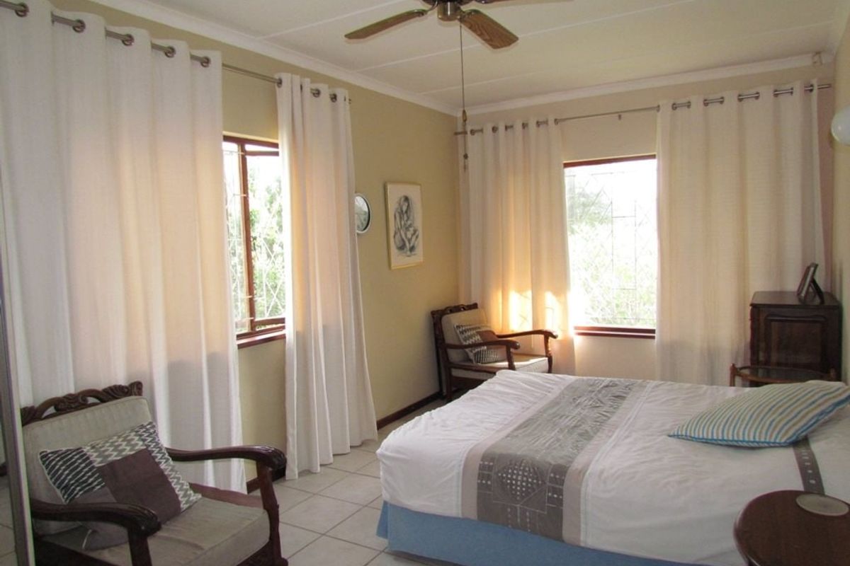 A well-lit bedroom featuring tiled flooring, a ceiling fan, and windows fitted with security bars, offering a comfortable and functional living space.