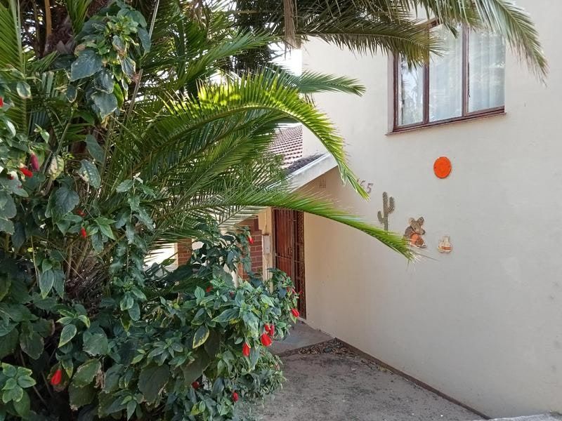 Front entrance area of the house featuring a security gate, tiled roof section, and mature garden foliage partially obscuring the facade.