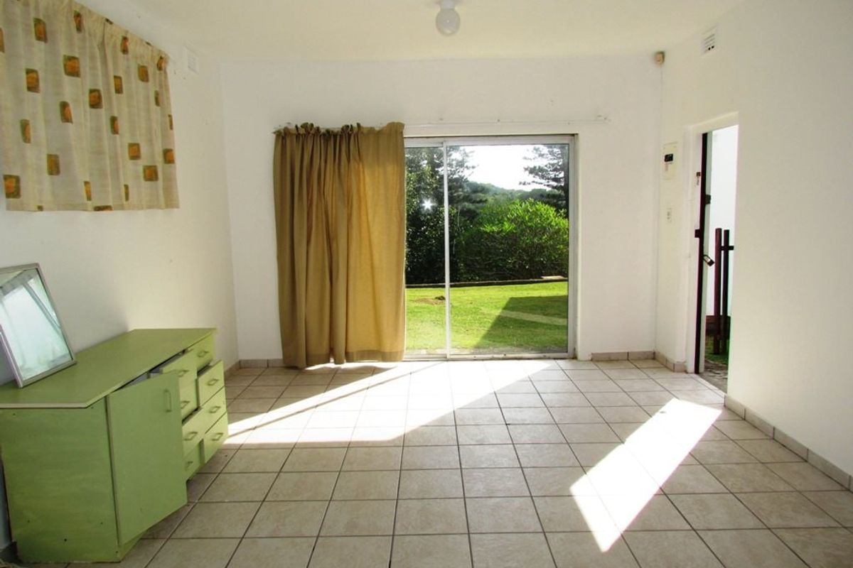 A bright, open-plan living area featuring neutral tiled flooring and a large sliding glass door providing direct access to the garden.