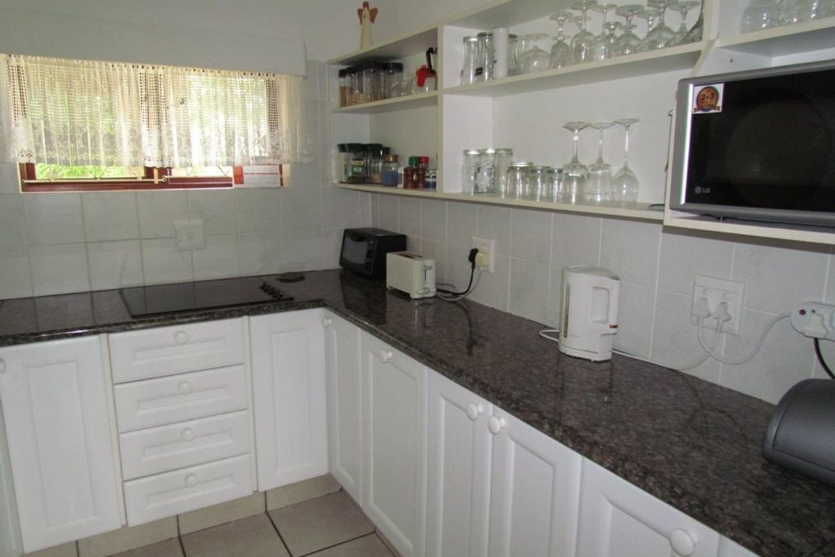 A functional kitchen featuring white cabinetry, granite countertops, ceramic tile flooring, and built-in appliances including a hob and microwave.