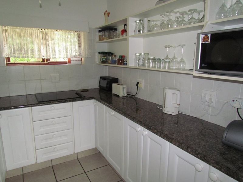 A functional kitchen featuring white cabinetry, granite countertops, ceramic tile flooring, and built-in appliances including a hob and microwave.