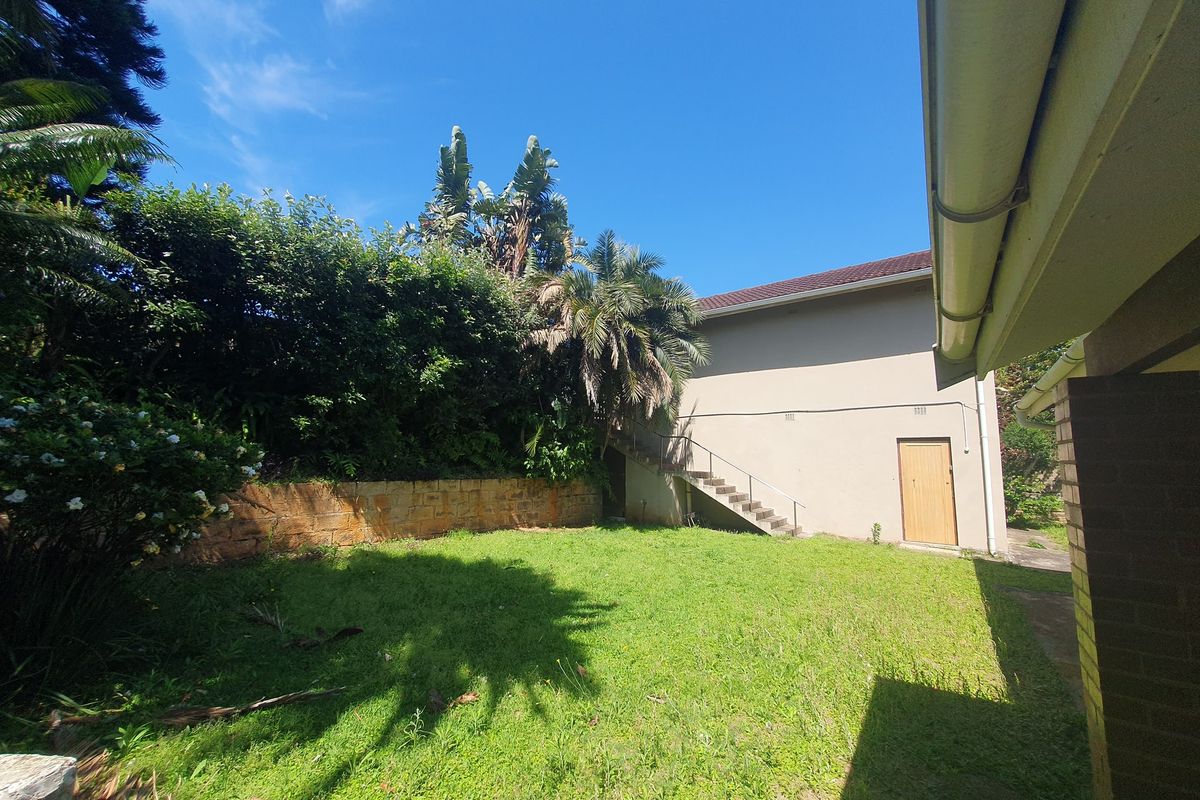 A rear garden area featuring a stone retaining wall, an external staircase leading to an upper level, and established landscaping.