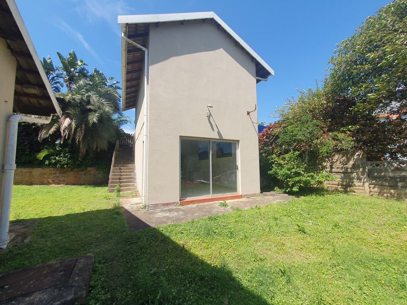 Rear view of the property featuring a sliding glass door, external concrete staircase, and a private garden area with a retaining wall.