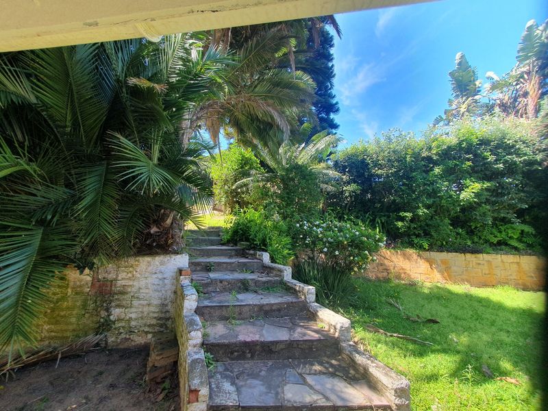 A garden area featuring stone stairs leading to an upper level, bordered by a stone retaining wall and established tropical landscaping.