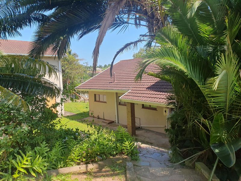 Rear view of the property featuring a tiled roof, brick pillar support, and a garden pathway leading to the house entrance.