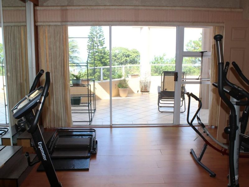 A home gym space featuring laminate flooring, a mirrored wall, and large sliding glass doors providing access to an outdoor balcony area.