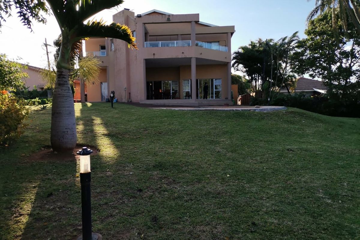 Rear view of a multi-level residential property featuring a spacious lawn, covered patio, and upper-level balconies with glass balustrades.