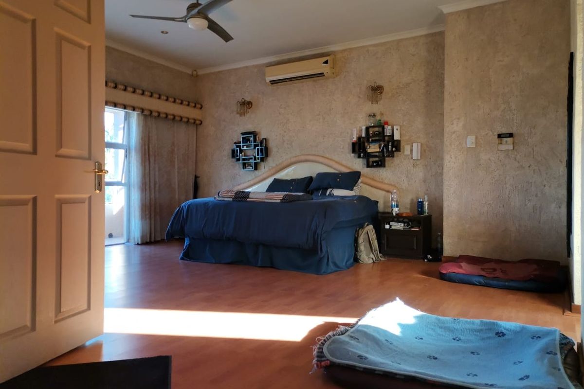 Spacious bedroom featuring laminate flooring, a ceiling fan, and a wall-mounted split-system air conditioner with textured wall finishes.