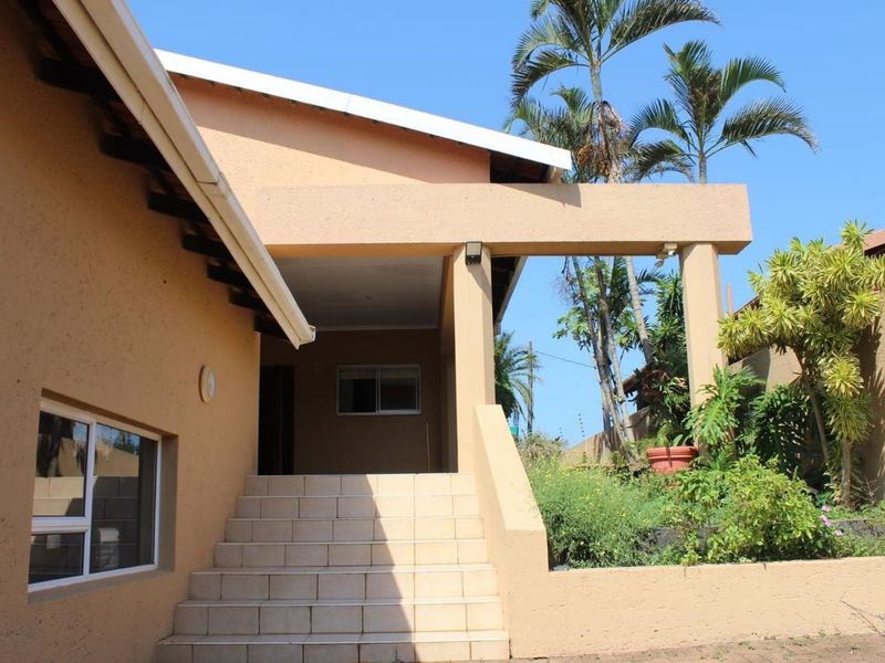 Front entrance of the house featuring a covered porch, tiled staircase, and plastered exterior walls with established garden surroundings.