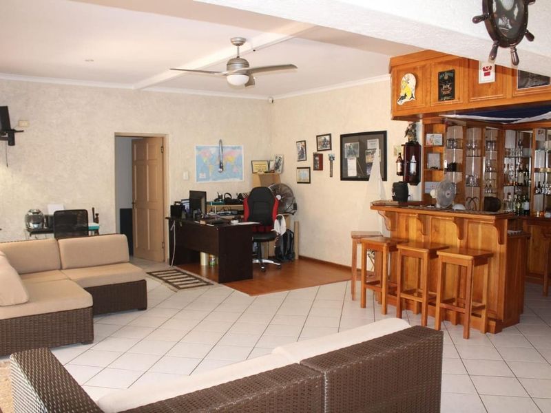 Open plan living area featuring a built-in wooden bar, tiled and laminate flooring, and a ceiling fan, offering a versatile entertainment space.
