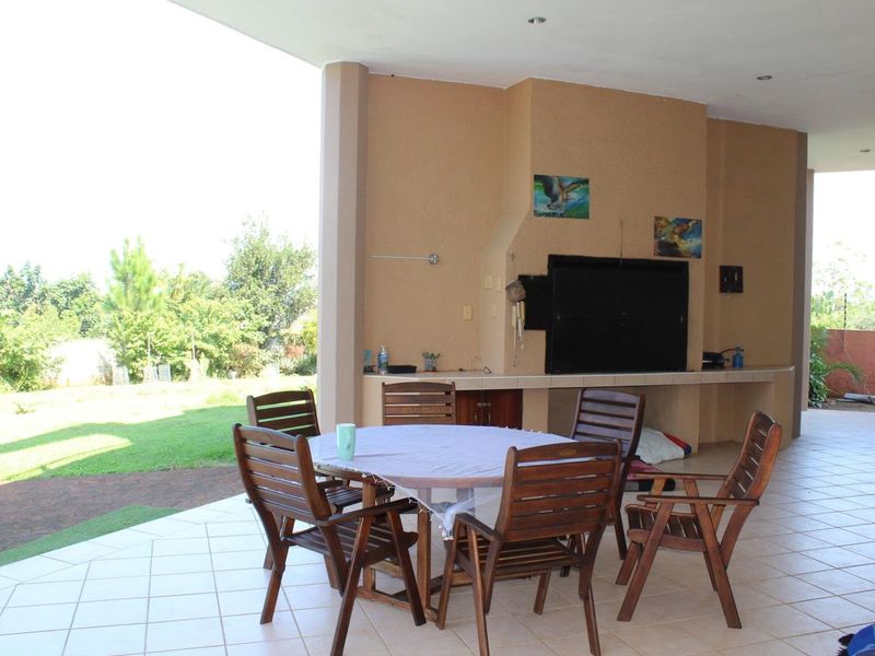 Covered patio area featuring a built-in braai, tiled flooring, and recessed lighting, offering a functional space for outdoor dining and entertainment.