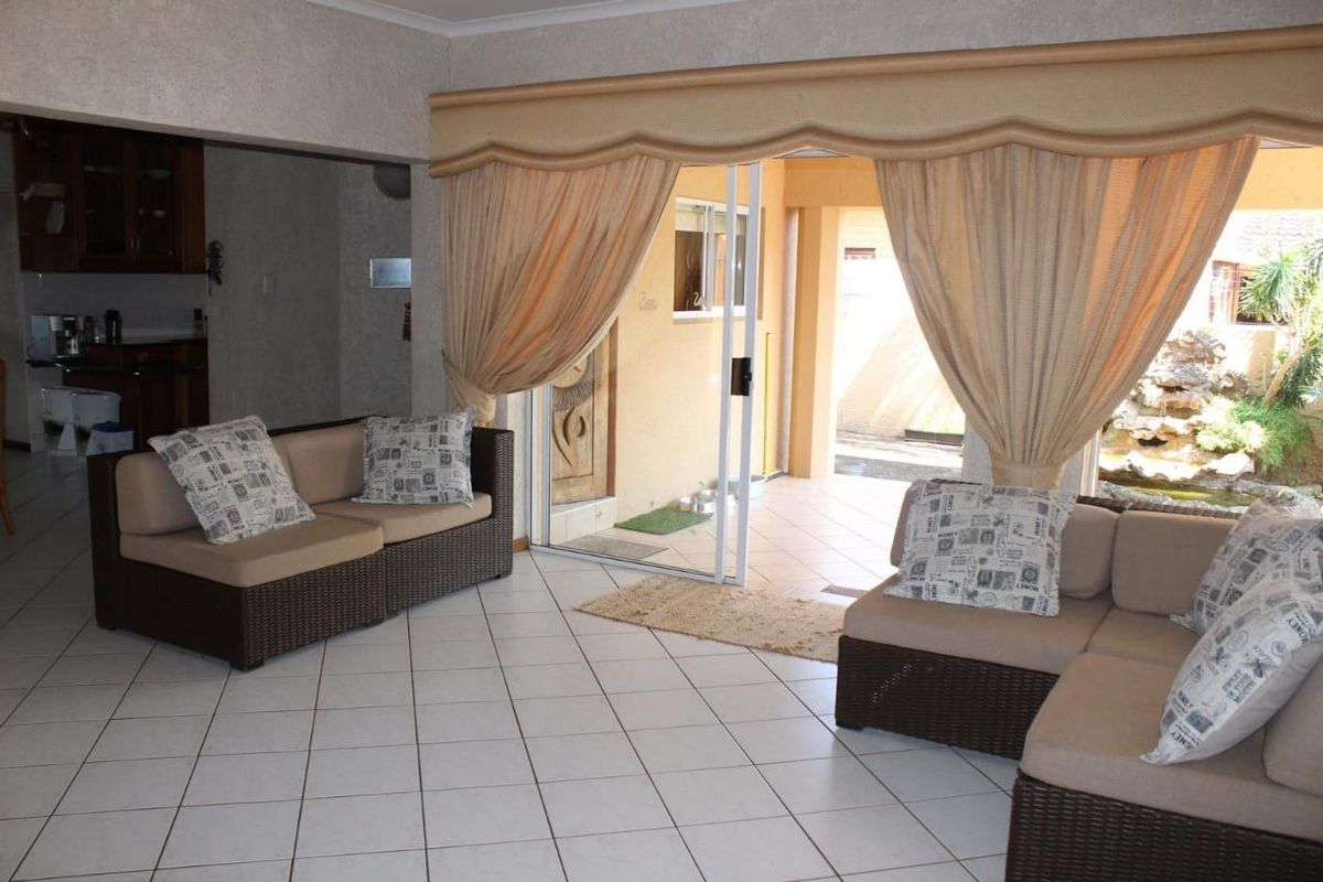 A living room featuring tiled flooring and a sliding glass door providing access to an outdoor patio area, with an adjacent kitchen space.