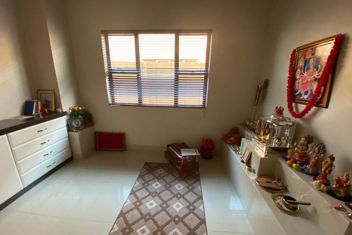 A multi-purpose room featuring tiled flooring, a built-in display ledge, and venetian blinds, currently utilized as a prayer room.