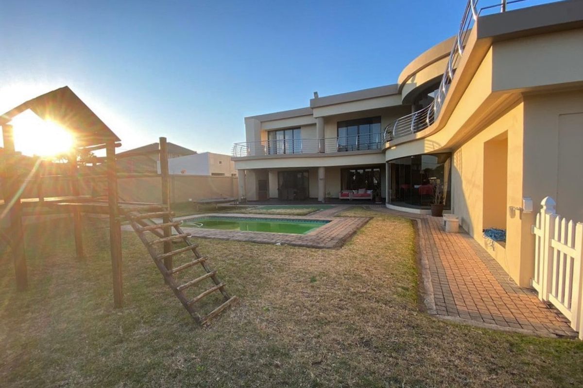 Rear view of a modern multi-story house featuring a swimming pool, paved patio area, and upper-level balcony with stainless steel railings.