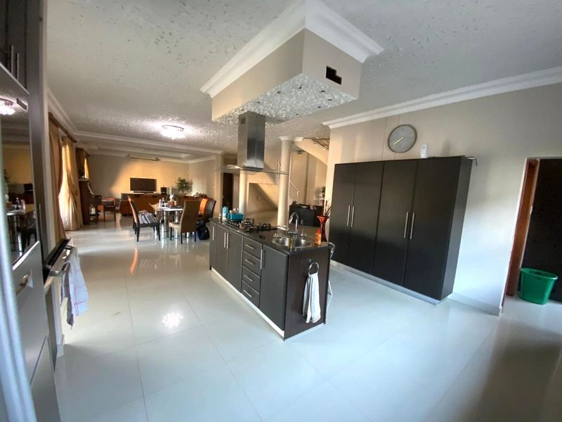 Spacious open-plan living area featuring a central kitchen island with gas hob, extractor fan, and modern dark cabinetry, flowing into the dining and lounge space.