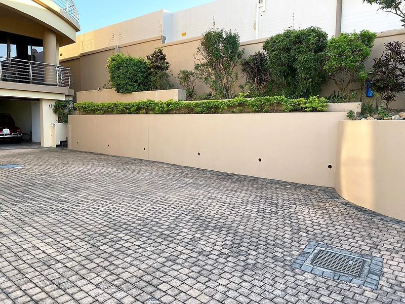 A well-maintained paved driveway leading to an integrated garage, featuring a tiered retaining wall with established landscaping and secure perimeter fencing.
