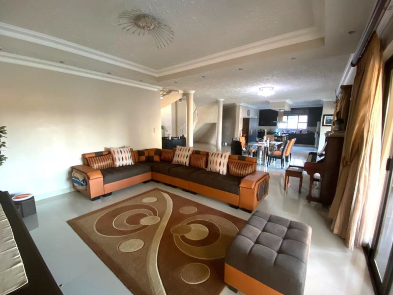 Spacious open-plan living and dining area featuring tiled floors, decorative recessed ceilings with cove lighting, and structural columns leading to the kitchen.