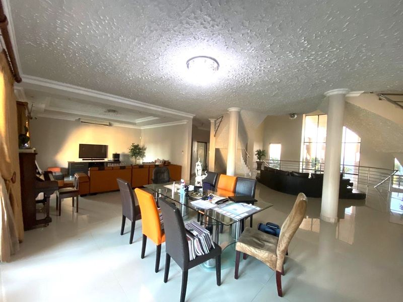 Spacious open-plan living and dining area featuring structural columns, a central staircase, and tiled flooring, offering a versatile layout for modern living.
