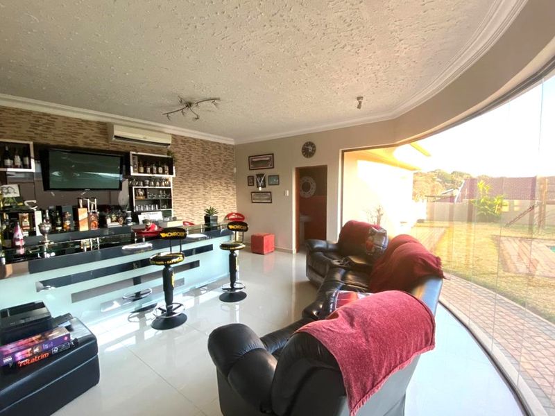 A spacious entertainment bar area featuring a built-in counter, tiled flooring, and a large curved glass wall providing natural light and garden views.