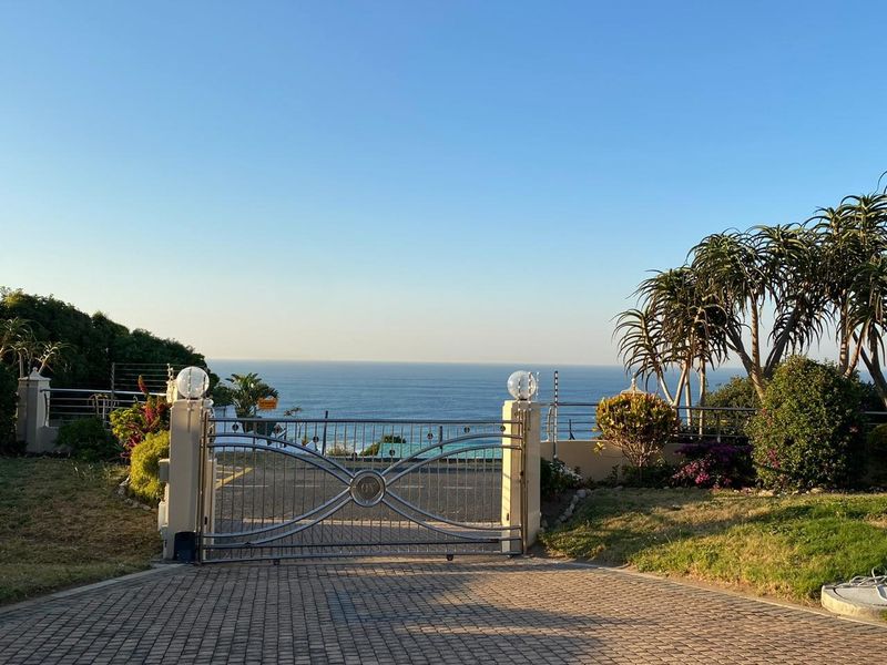 Front entrance featuring a decorative metal driveway gate, masonry pillars with lighting, and a paved driveway overlooking the ocean.