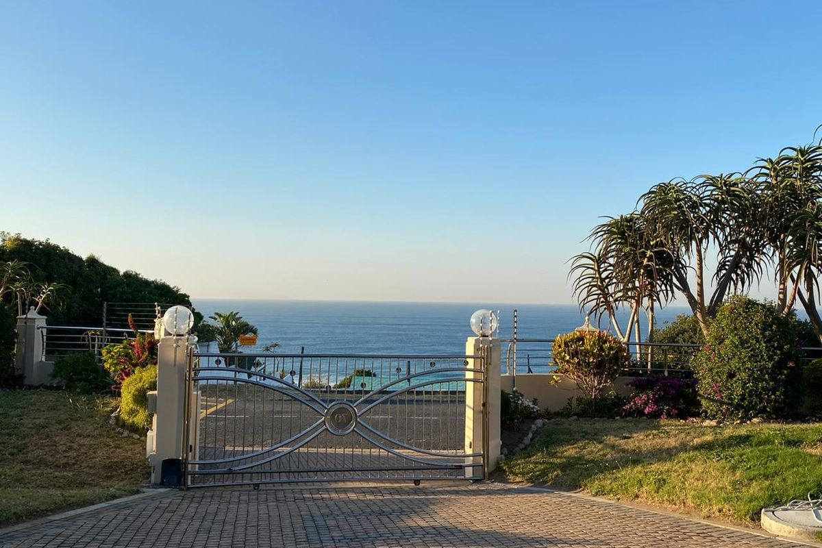Front entrance featuring a decorative metal driveway gate, masonry pillars with lighting, and a paved driveway overlooking the ocean.